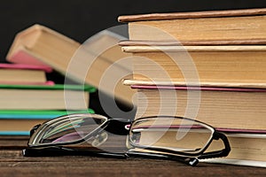 A stack of books and glasses on a brown wooden table and on a black background. Old books. Education. school.