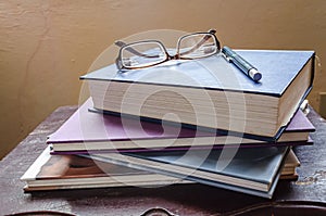 Stack Of Books With Glasses And Pen At Top