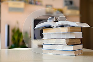 Stack of books and glasses on the table in the room. Open book with glasses.
