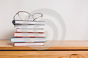A stack of books and glasses on wooden table. Mock up with education and reading concept. Literature for learning, development and