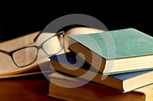 Stack of books in hard cover with glasses and black background