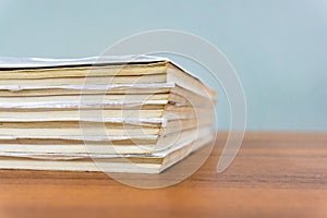 A stack of books are lying on a brown table, documents are stacked close-up