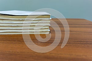 A stack of books are lying on a brown table, documents are stacked close-up