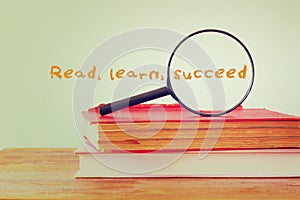 Stack of books and magnifying glass with the phrase learn read succeed. education concept