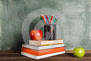 A stack of books and office supplies and two apples on the background of the school board.