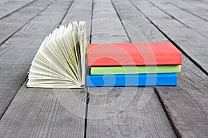 Stack of books and open book with fanned pages on wooden floor a