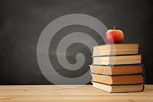 stack of books over wooden desk in front of blackboard.