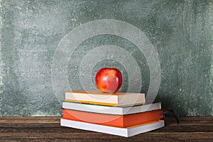 A stack of books and a red apple on the background of the school board.