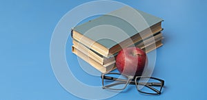 stack of books, red apple and glasses isolated on colorful surface, simple abstract study concept