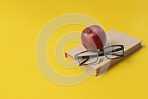 stack of books, red apple and glasses isolated on colorful surface, simple abstract study concept