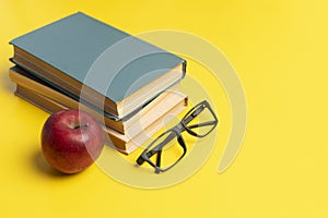 stack of books, red apple and glasses isolated on colorful surface, simple abstract study concept