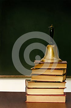 Stack of books and school bell on desk