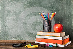 a Stack of books and stationery and a red apple on the background of the school board.