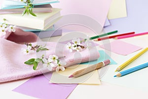 A stack of books, textbooks, pencils, notepads and twigs of cherry blossoms on a table, against a background of colored paper in p