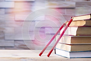 Stack of books and two red wooden pencils on wooden background, back to school concept