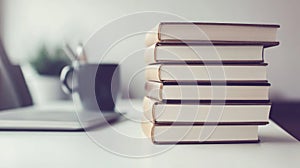 A Stack of Books on a White Table with a Laptop and Cup in the Background