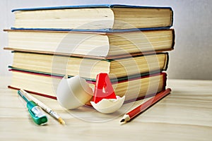 A stack of books writing materials and a split chicken egg with the letter a inside on the table concept knowledge education