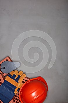 Stack of bricks with masonry trowel, construction hard hat, gloves on gray concrete background. Top view. Construction concept