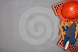 Stack of bricks with masonry trowel, construction hard hat, gloves on gray concrete background. Top view. Construction concept