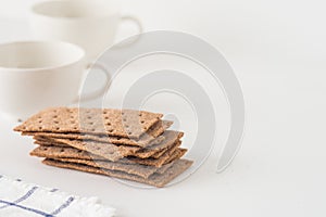 Stack of brown rye crispy bread Swedish crackers with two cups and piece of cloth on white background with space for text