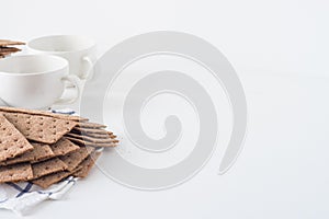 Stack of brown rye crispy bread Swedish crackers with two cups and piece of cloth on white background with space for text