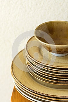 Stack of brown speckled glazed earthenware ceramic plates dishes and bowls on wooden table. White wall background