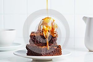 Stack of brownie squares with scoop of ice cream and caramel, white background