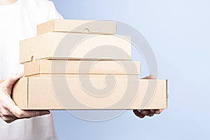 Stack of cardboard boxes in female hands. Blank brown parcel boxes on light blue background. Packaging, shopping, free