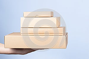 Stack of cardboard boxes in female hands. Blank brown parcel boxes on light blue background. Packaging, shopping, free