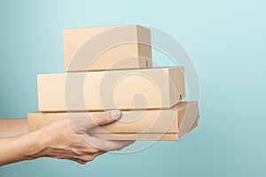 Stack of cardboard boxes in female hands. Blank brown parcel boxes on light blue background. Mock up. Packaging