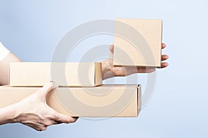 Stack of cardboard boxes in female hands. Woman showing small blank brown box. Blank parcel boxes on light blue