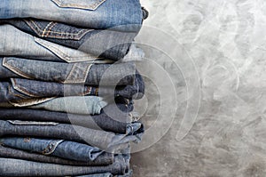 A stack of carelessly folded jeans on gray background. Close-up of jeans in different colors. Copy space