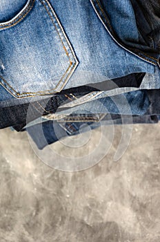 A stack of carelessly folded jeans on gray background. Close-up of jeans in different colors. Denim background