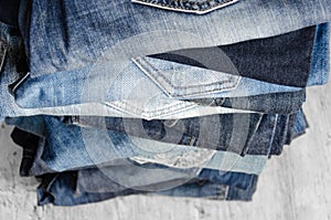 A stack of carelessly folded woman`s jeans on gray background. Close-up of jeans in different colors. Selective focus photo