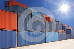 Stack of cargo containers at container yard with sunbeam