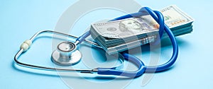 Stack of cash dollars and stethoscope on blue background. The concept of medical strechevka or expensive medicine, doctors salary