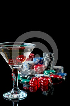 Stack of Casino gambling chips, glass of martini vermouth and red dices isolated on reflective black background
