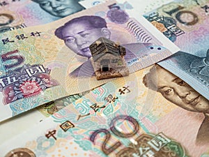 Stack of Chinese Yuan banknotes with a small miniature house on them