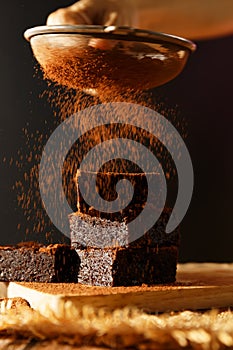 Stack of chocolate brownies fudge on wooden butcher with  blur grille Is sprinkling cocoa powder on top