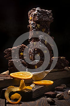 A stack of chocolate brownies on wooden background with orange peels and pistachio nuts