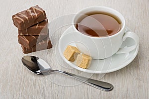 Stack of chocolate candies, cup of tea, sugar and teaspoon