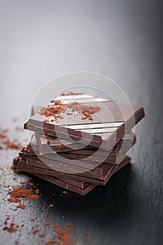 Stack of chocolate chunks on a dark stone background with cocoa