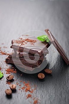 Stack of chocolate chunks with mint on a dark stone background with cocoa