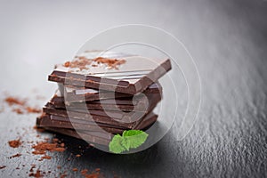 Stack of chocolate chunks with mint on a dark stone background with cocoa