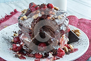 Stack of chocolate pancakes topped wtih cherry and walnuts, sprinkled with powdered sugar and drizzled with maple syrup. Gourmet B