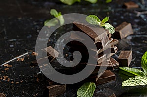 Stack of chocolate pieces with a leaf of mint on dark background