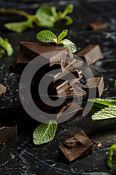 stack of chocolate pieces with a leaf of mint on dark background