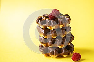 Stack of chocolate waffles with raspberries. Close up and yellow background.