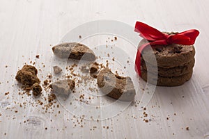 A stack of Christmas chocolate cookies tied a red ribbon. Broken cookies, a lot of crumbs on the table.