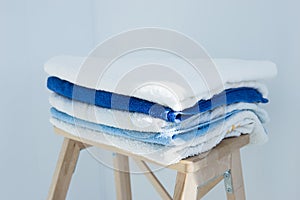Stack of clean bath towels colorful cotton Terry textile stacked on wooden chair near white wall pile concept closeup